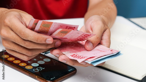 a man's hand is counting rupiah money with a calculator and notes