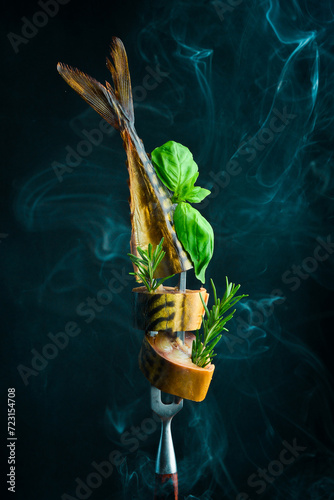 Smoked mackerel fish on a metal fork. Pieces of juicy smoked fish. On a black background. photo