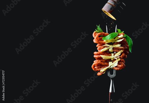 Dry smoked Kabanos or cabanossi traditional Polish thin sausages on a metal fork. Kabanos Close up on a black background. photo