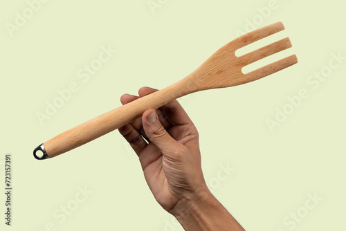 Black male hand holding a wooden cooking fork on light green background.