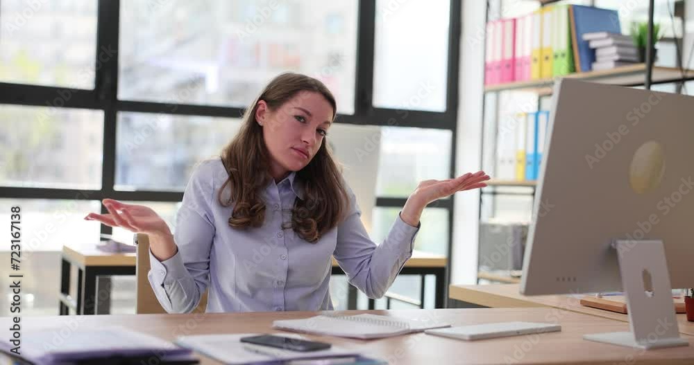 Unsure woman working at computer sits at workplace and shrugs Unsure woman working at computer sits at workplace and shrugs