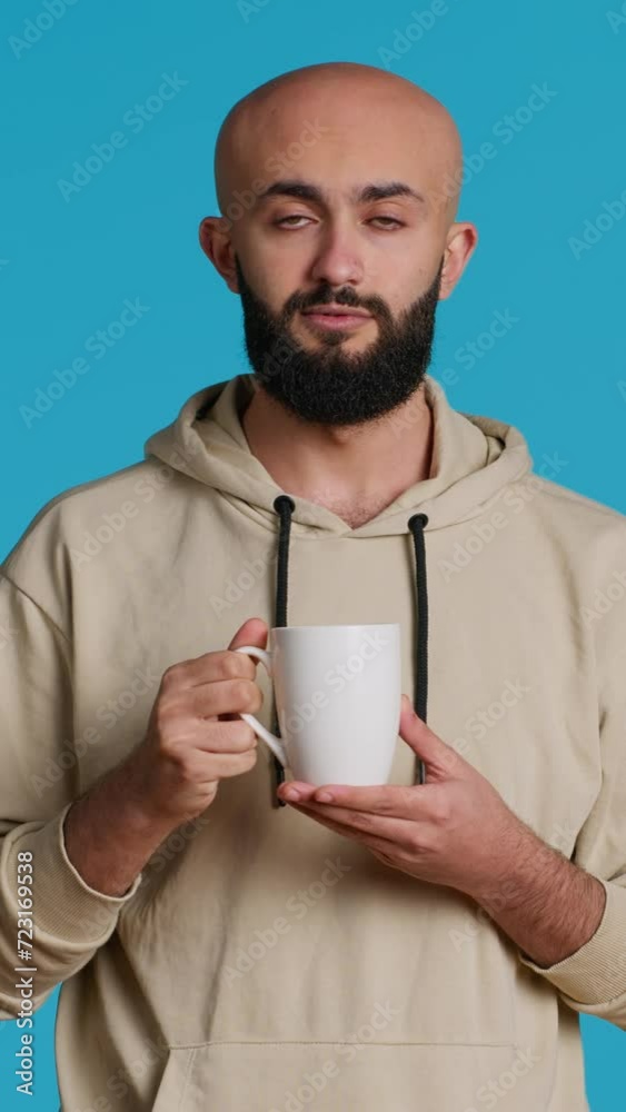 Vertical Video Muslim person enjoying fresh caffeine aroma in studio, drinking cup of coffee and standing over blue background. Middle eastern adult smelling beverage and taking a sip. Camera 1. Vertical Video Muslim person enjoying fresh caffeine aroma in studio, drinking cup of coffee and standing over blue background. Middle eastern adult smelling beverage and taking a sip. Camera 1.