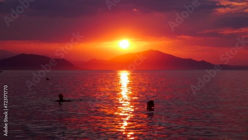 Sunset on the beach in Peki, Greece. A fiery red sky with a setting sun and a sea that reflects red. You can see the heads of two bathers enjoying the sea photo