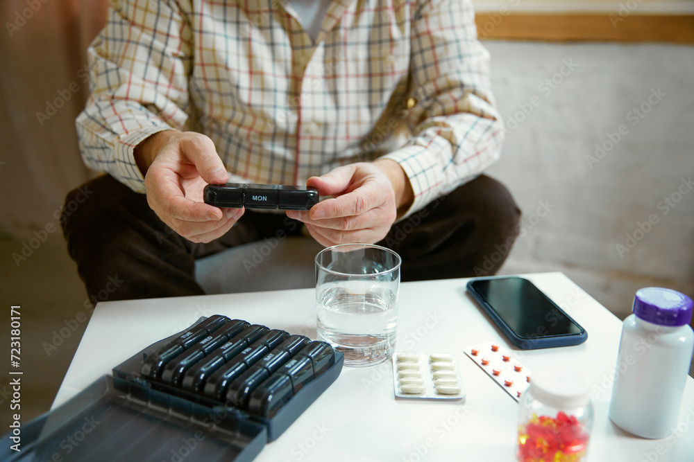 Fototapeta premium Hands of a senior man holding pill box, medication containers labeled with days of week. Organizer for daily pills and vitamins. Concept of health and medical care, aging, medicine, treatment