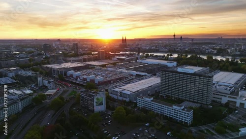 Aerial flight with sun backlit over the city of cologne with sunset and colorful sky. There is evening traffic on Highway. Drone move left