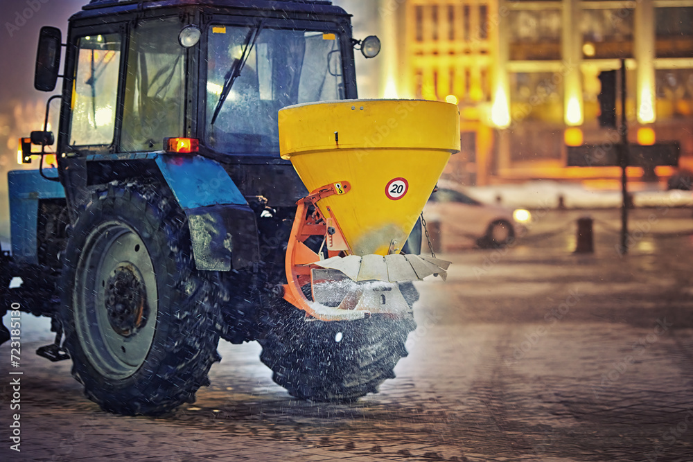 Salt spreader machine work at night, salting paving slabs, tactor spreading rock salt on