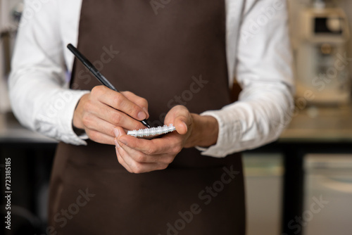 Pizzeria worker in apron making notes for order preparation