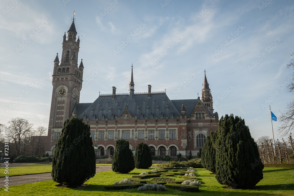 International Court of Justice The Hague, Netherlands on clear sunny day shot from street level. shot of clock tower main entrance with front garden and pruned trees International Court of Justice The Hague, Netherlands on clear sunny day shot from street level. shot of clock tower main entrance with front garden and pruned trees