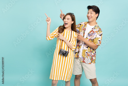 Young Asian couple in summer outfits standing and pointing to copy space isolated on green background