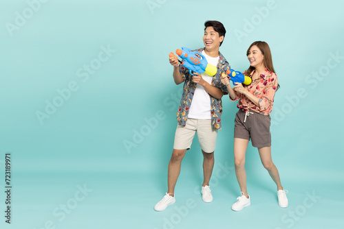 Young Asian couple in summer outfits holding water guns plastic for Songkran festival in Thailand isolated on green background