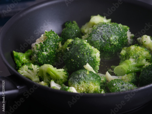 Frozen broccoli cooking in a frying pan. Close up.