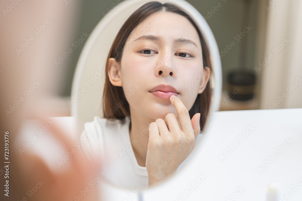 Lip care concept, worried asian young woman finger touching lips in front of mirror after applying lipstick balm on dry mouth from natural beauty product, skincare routine, makeup and cosmetics. Lip care concept, worried asian young woman finger touching lips in front of mirror after applying lipstick balm on dry mouth from natural beauty product, skincare routine, makeup and cosmetics.