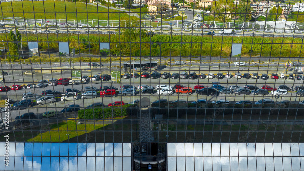 Reflected in the glass of a building is an office car park.