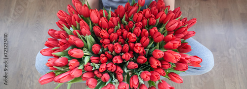 A banner with a bunch of red tulips, which is held in the hands of unrecognisable person with a copy space. Top view of a large bouquet of red tulips. 