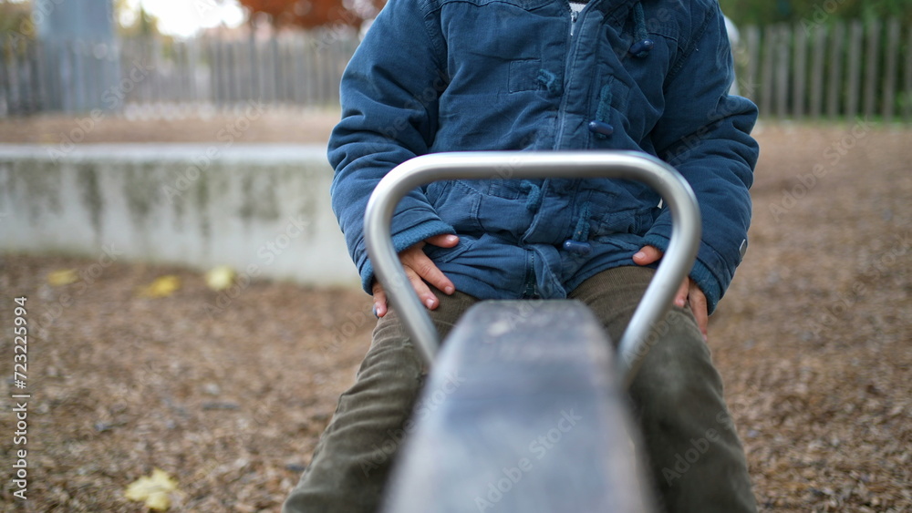 Obraz premium Joyful child plays at park on top of seesaw, Active 3 year old boy kid wearing blue jacket enjoys autumn day outdoors