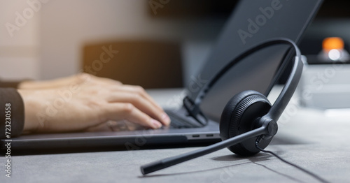 close up headset with employee man hand type work on keyboard laptop at desk for advise or share information to customer for hotline call center and service provider concept photo