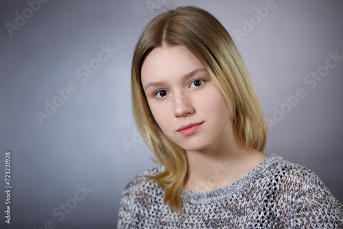 Cute blonde teenage girl on a gray background.