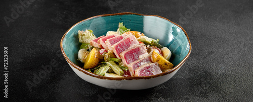 Seared medium-rare tuna Salad Nicoise, with potatoes, greens, and eggs in a teal bowl