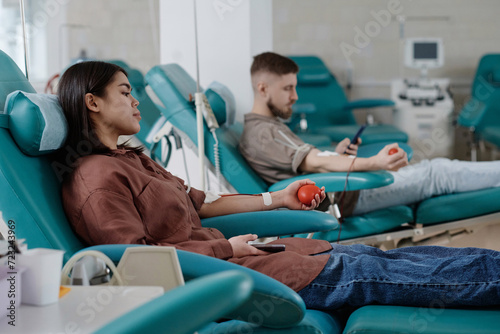 Male and female blood donors sitting in clinic armchairs during transfusion process, focus on woman