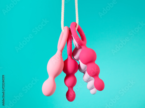 Set of pink sex toys hanging on a rope over blue cyan background