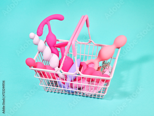 A lot of female pink sex toys in shopping basket over turquoise background