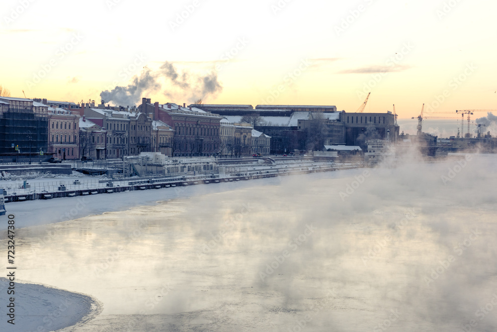 Steam coming from a frozen river near the embankment with residential houses