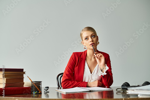 appealing young woman with blonde hair in vibrant attire sitting at table and taking notes at office