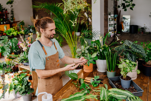 Positive young male gardener wearing apron takes care of indoor plant,