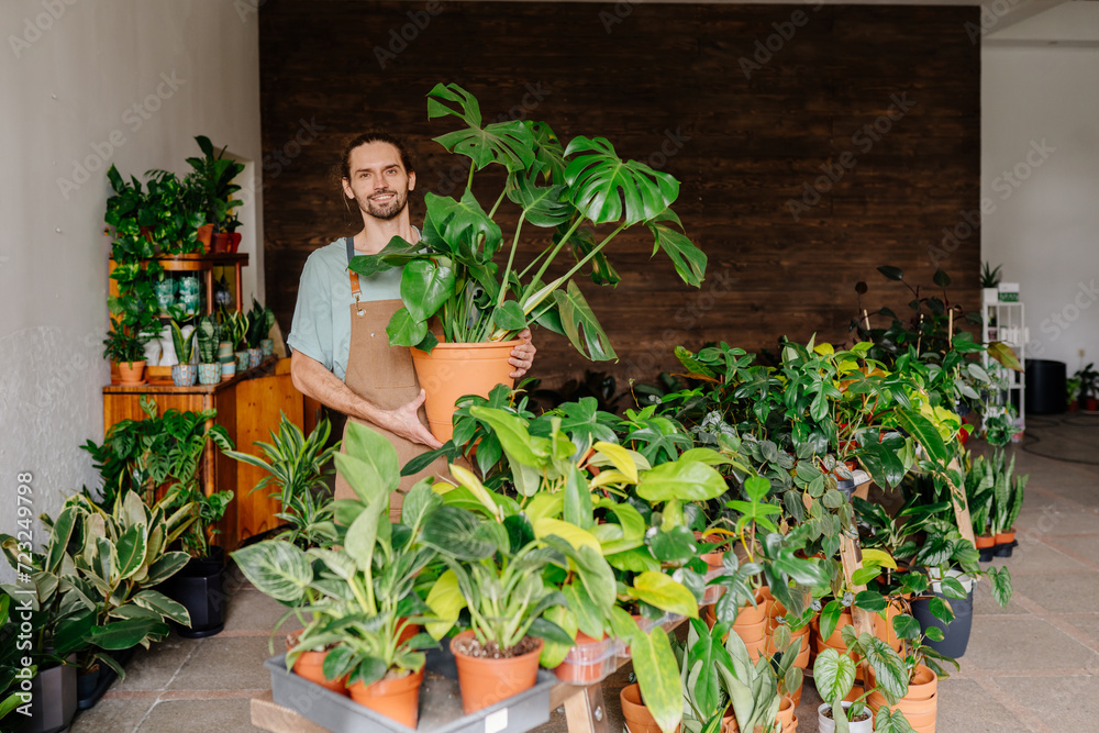 Portrait of a young asian woman business owner holding many house plants smiling and looking at camera in a greenhouse. Gardener working in flower shop, plant store. Portrait of a young asian woman business owner holding many house plants smiling and looking at camera in a greenhouse. Gardener working in flower shop, plant store.