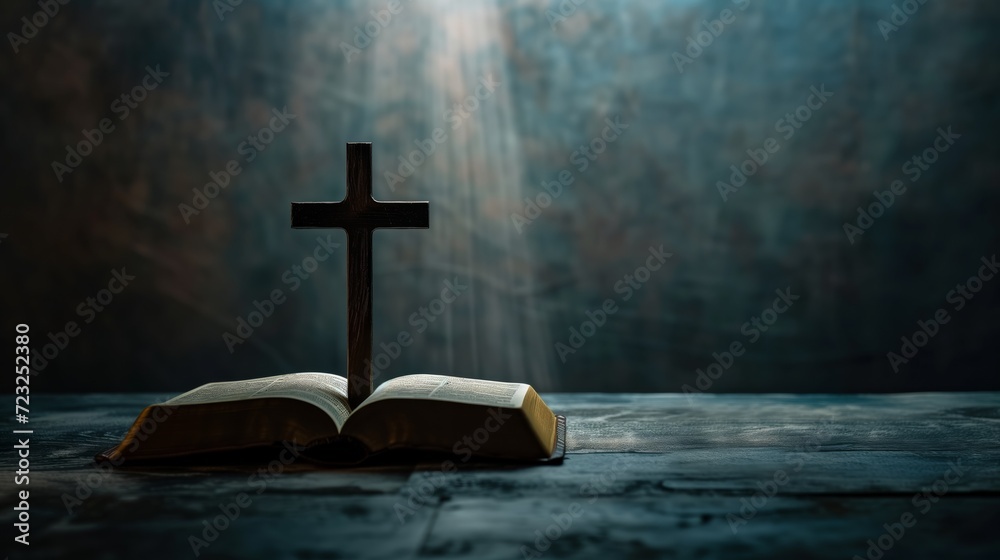 Holy cross, crucifix standing next to a bible on a dark background with rays of light directed from above
