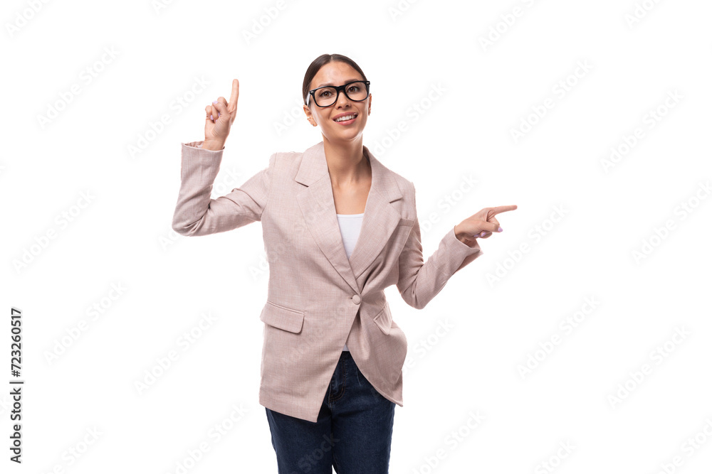 young caucasian woman with black hair gathered in a ponytail dressed in a beige jacket points with her hands to the space for advertising young caucasian woman with black hair gathered in a ponytail dressed in a beige jacket points with her hands to the space for advertising