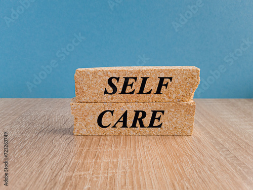 Take care of yourself symbol. Red text SELF CARE on brick blocks, beautiful red background, wooden table.