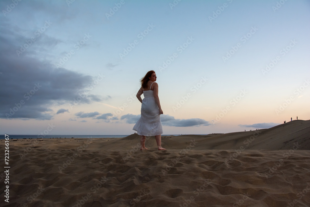 Young woman stands with her back in the sand dunes Young woman stands with her back in the sand dunes
