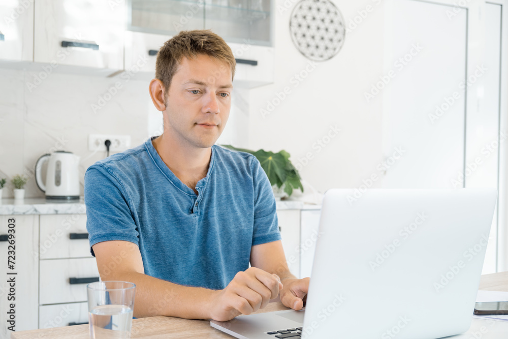 Young attractive man working on laptop online at home, using internet. Male freelancer using computer for distance work. Remote job. Modern technology