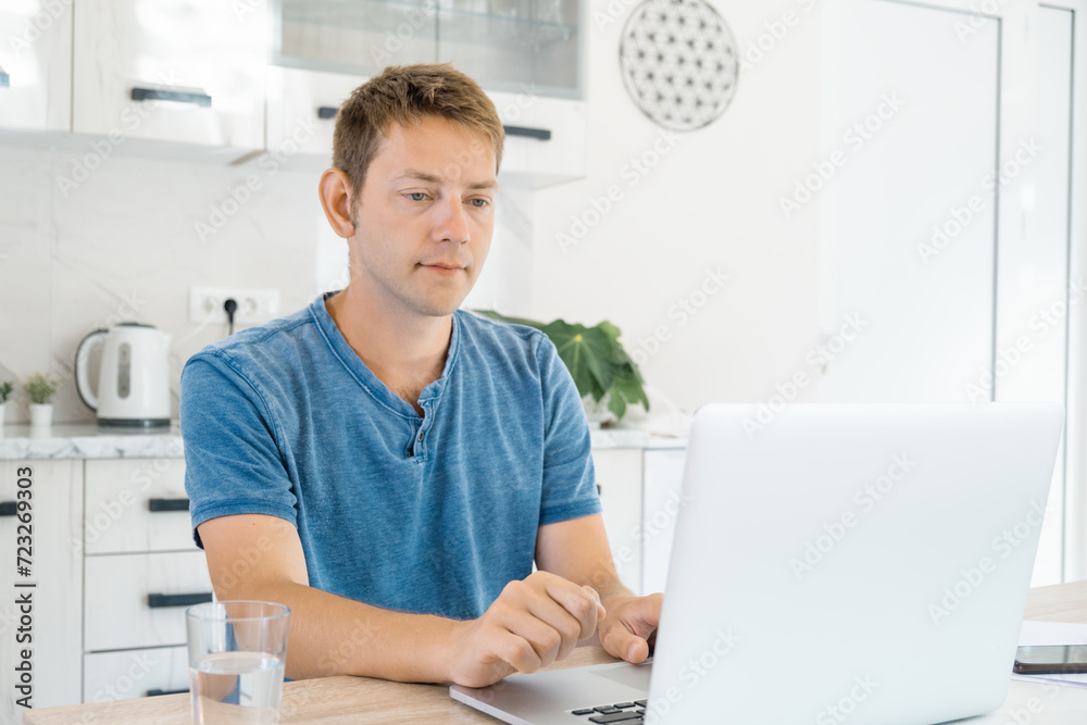 Young attractive man working on laptop online at home, using internet. Male freelancer using computer for distance work. Remote job. Modern technology Young attractive man working on laptop online at home, using internet. Male freelancer using computer for distance work. Remote job. Modern technology