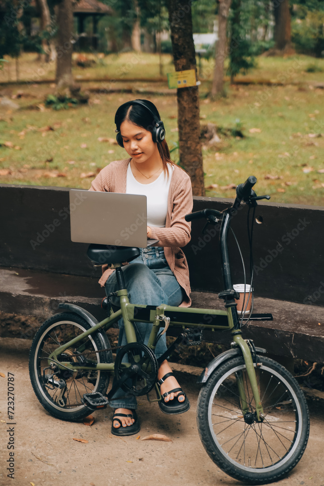 Fototapeta premium Happy young Asian woman while riding a bicycle in a city park. She smiled using the bicycle of transportation. Environmentally friendly concept.