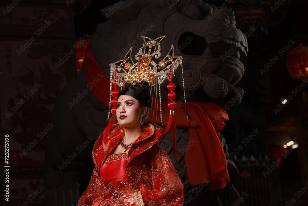 A charming Asian woman in Red ancient Chinese costume with a lion statue at a shrine