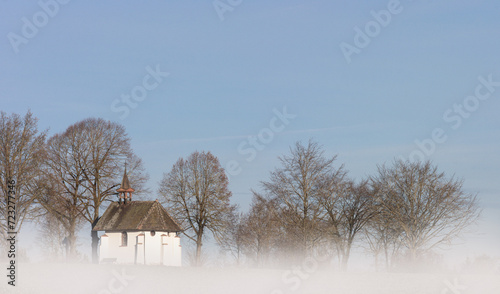 The St. Wendelin Chapel near Weigheim, enveloped in ground fog, shines in the sunlight. Through the blue sky, a picturesque scene of architecture and nature unfolds, timeless and harmonious. photo