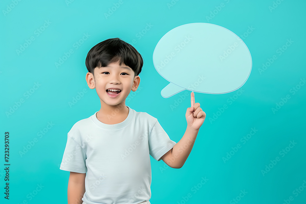 Portrait of cute Asian boy holding up empty speech bubble for text in studio background.