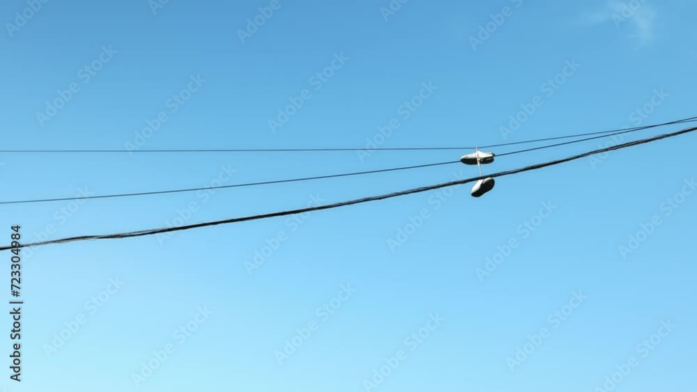 Sneakers caught on electric wires and hanging high off the ground against the blue sky swaying in Sneakers caught on electric wires and hanging high off the ground against the blue sky swaying in