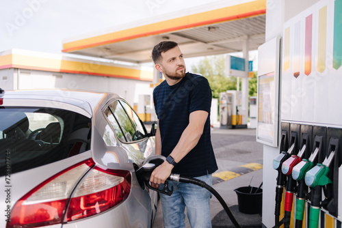 Bearded man refuelling car on gas station and looking into his smartphone. Man compares fuel prices 