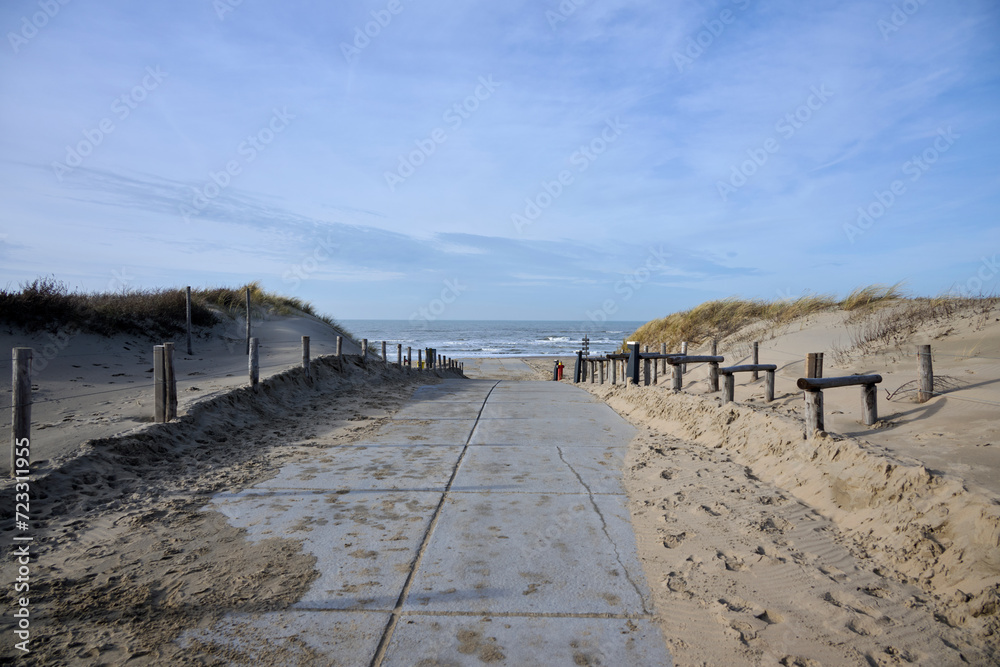 concrete path to the beach between the dunes to the lovely sea, with sun and blue sky