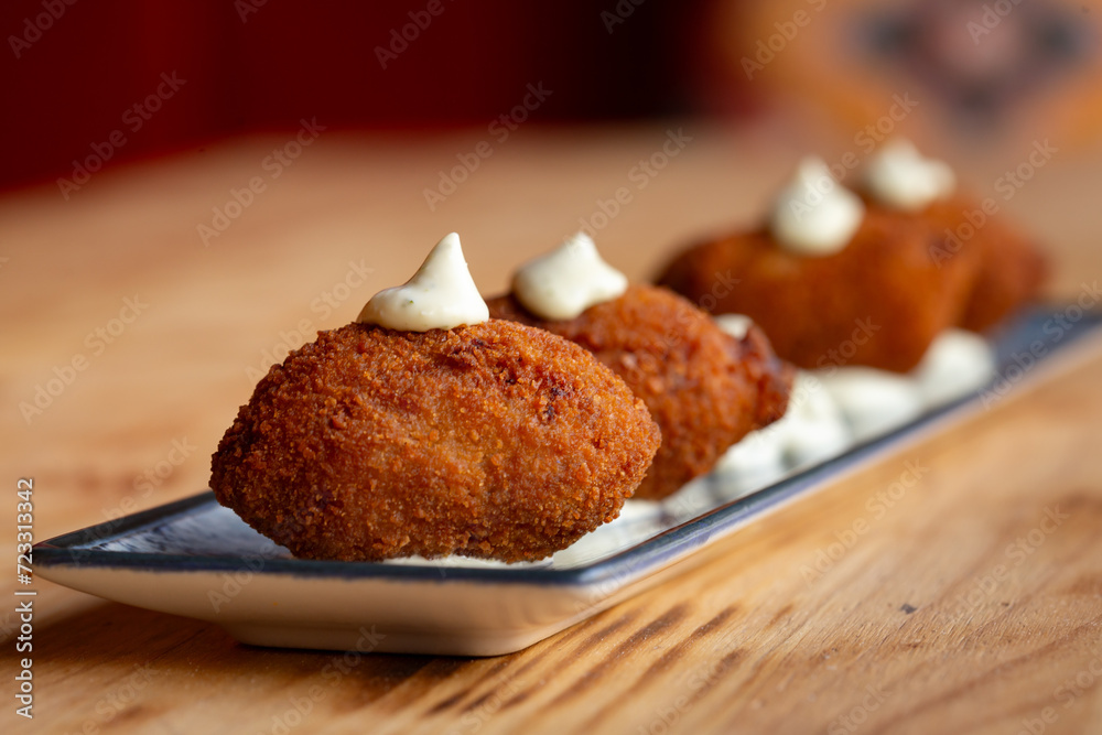Fototapeta premium Plato de apetitosas croquetas con salsa mayonesa y ali oli en la mesa de madera de un restaurante español