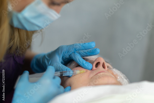 A beautician wearing a surgical mask gives the patient an injection.