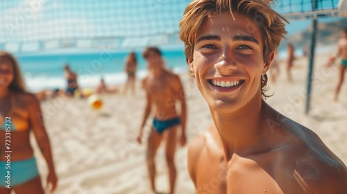 A young guy smiling looks at the camera. He plays beach volleyball with friends