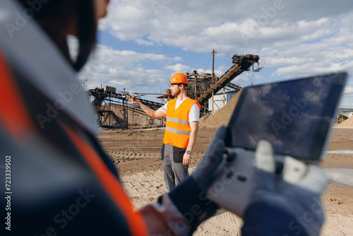 Concept industrial inspection surveillance from pilot engineer. Two operator workers piloting drone at industry open pit mine sand quarry