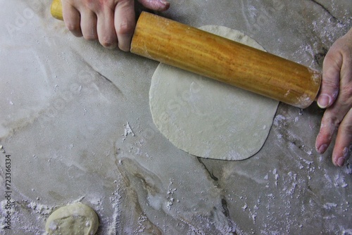 on the kitchen table, women's hands roll out dough with a rolling pin. several round pieces of dough and a prosky piece for stuffing it with meat are visible.