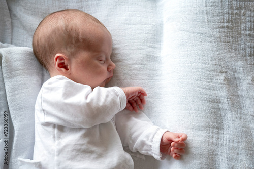 Close Up Photography of Peaceful newborn baby sleeping on its left side, radiating innocence and calm. Sleeping peacefully on its side, wearing white pajama on white bed. White background. 