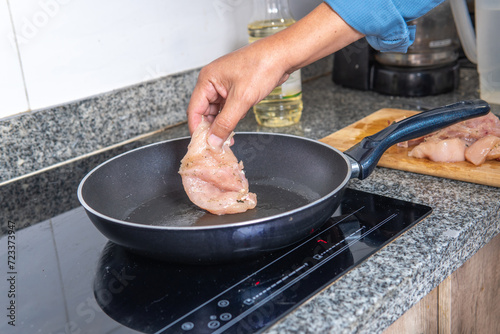 man's hand placing a piece of chicken in the pan on an induction cooker photo