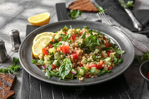 Plate with delicious tabbouleh salad and lemon slices on table, closeup